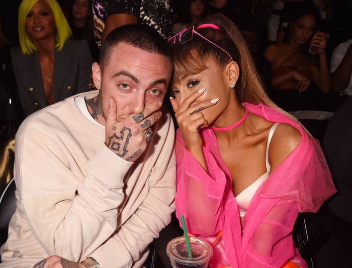 Mac Miller and Ariana Grande sitting together and covering their mouths with their hands as they pose for a photo