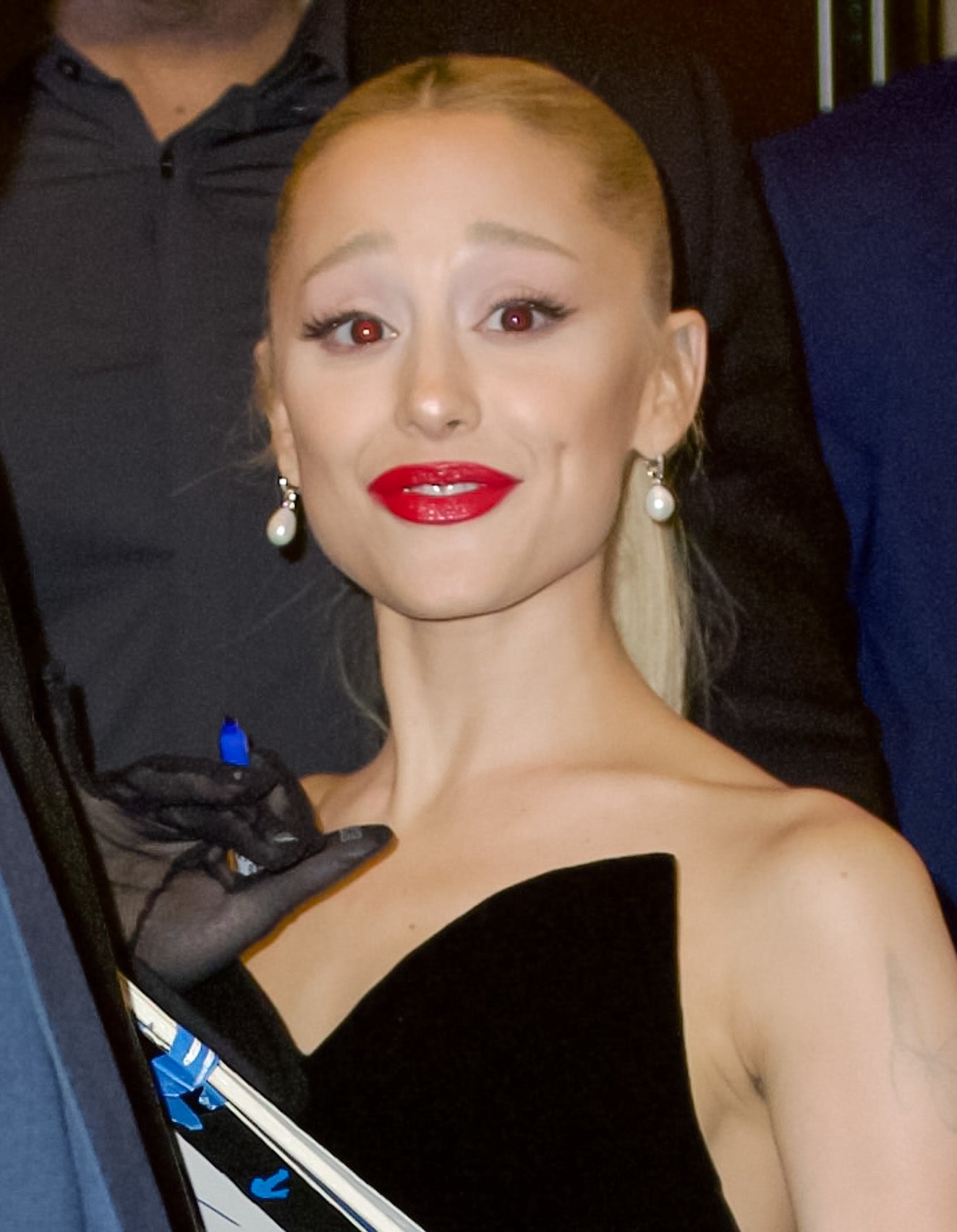 Ariana Grande with sleek bun, red lipstick, and black off-shoulder outfit smiling
