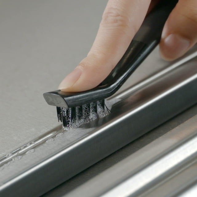 Hand cleaning a stove with a cleaning brush