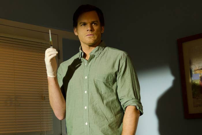 Man in casual shirt holding a syringe, standing indoors with serious expression