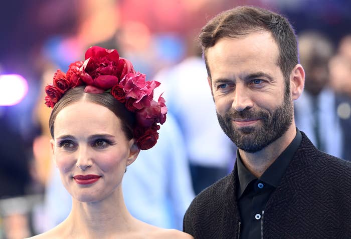 Natalie Portman and Benjamin Millepied smiling at an event; Natalie is wearing a floral headpiece and Benjamin is wearing a suit