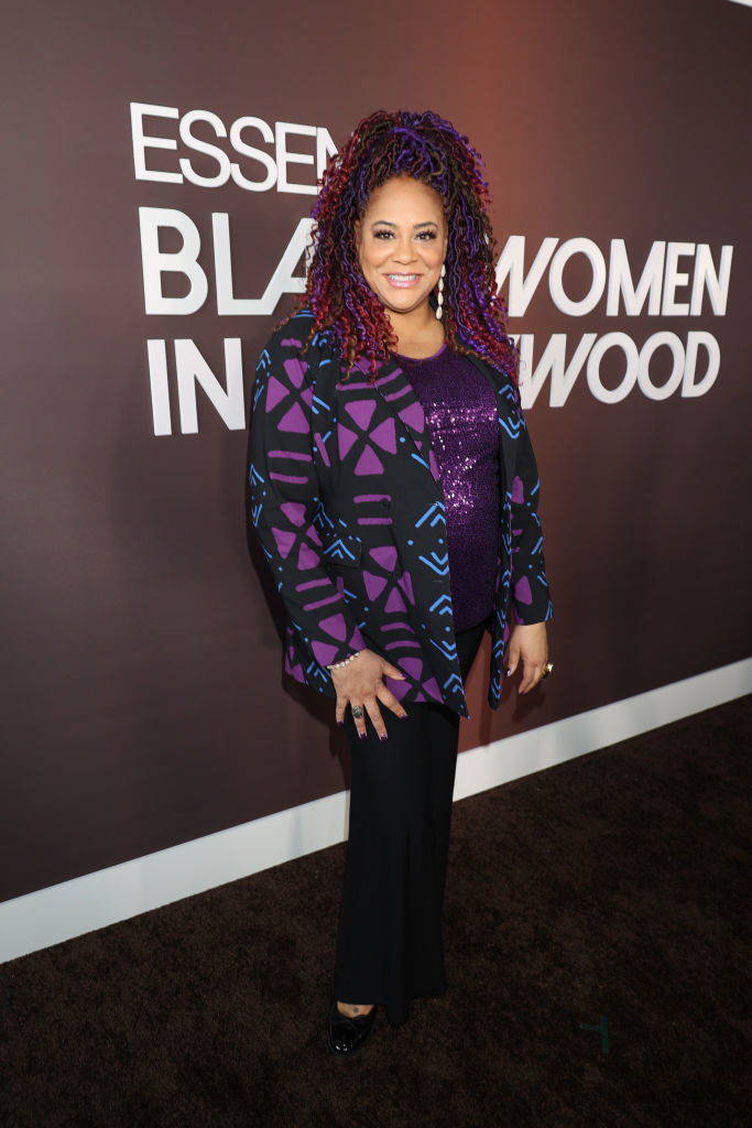 Kim smiles in a patterned jacket, top with sequins, styled hair, and pants