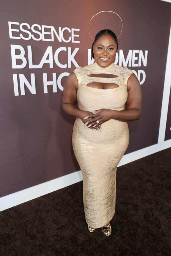 Dannielle stands on the red carpet wearing a fitted, cutout gown with halo hair accessory