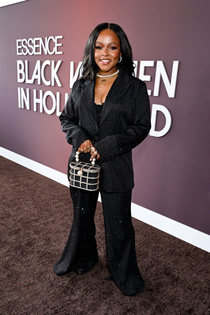 Gia smiles at the event in a sparkling pantsuit with flared-bottom pants and embellished handbag