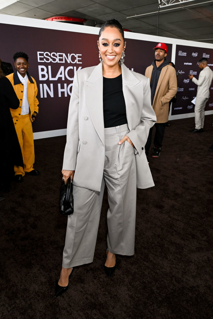 Tia at event in a relaxed suit holding a handbag and smiling for the camera