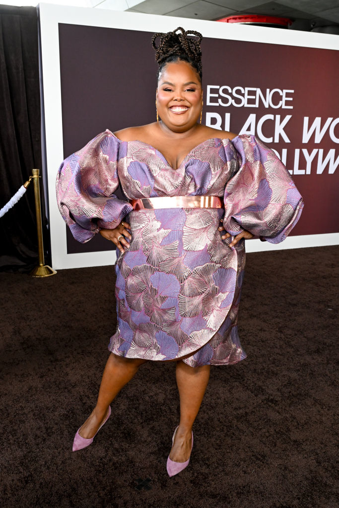 Danielle smiling in a short shiny floral-print dress with puffed sleeves and posing on the carpet