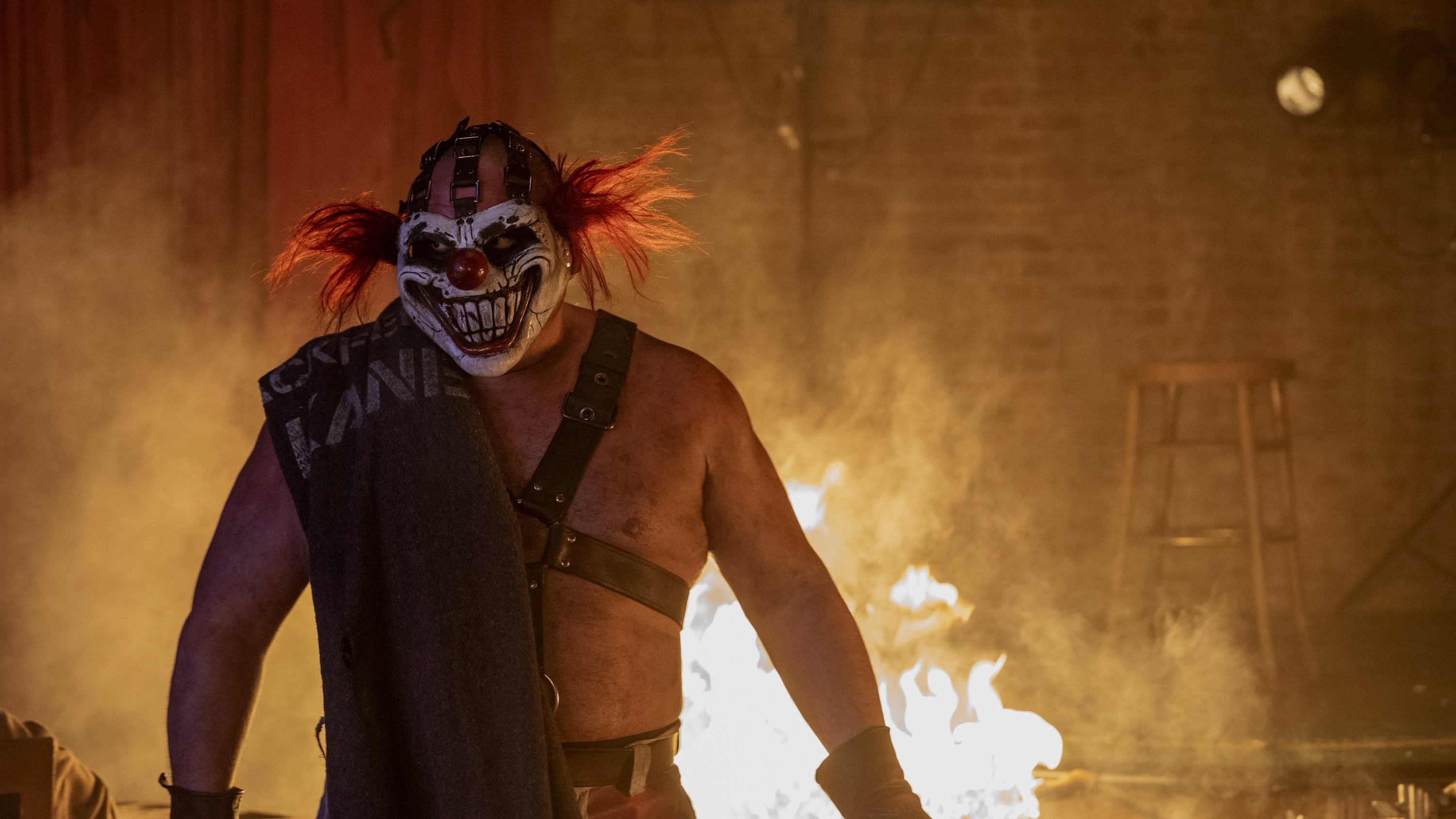 Person with a menacing clown mask and costume stands in front of flames on a stage