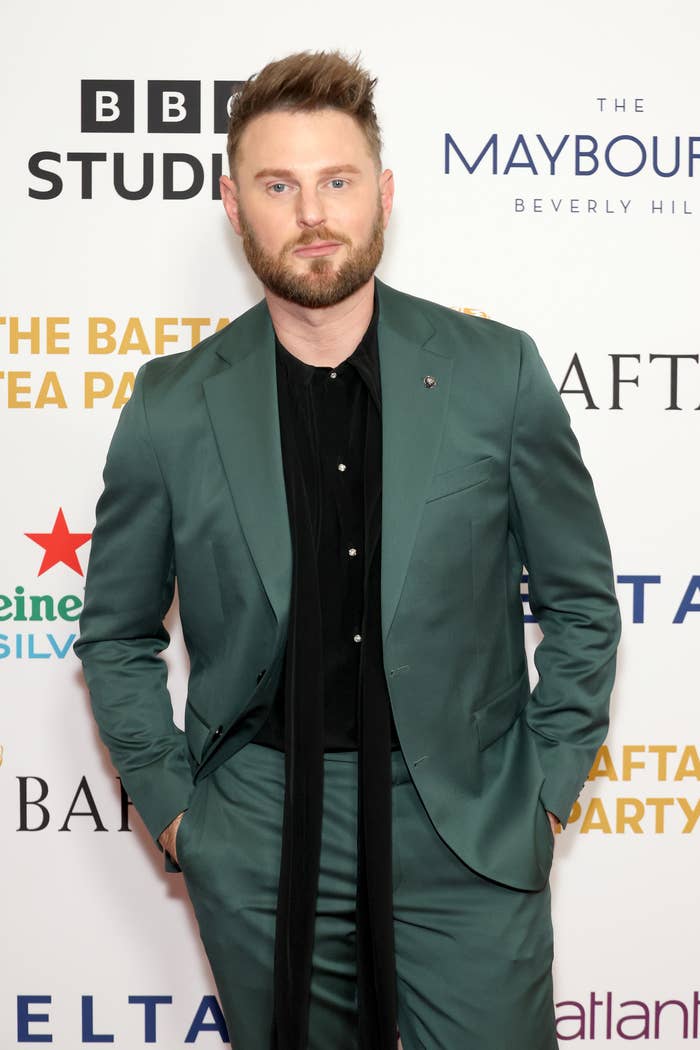 Bobby Berk in a suit and standing before a BAFTA event backdrop