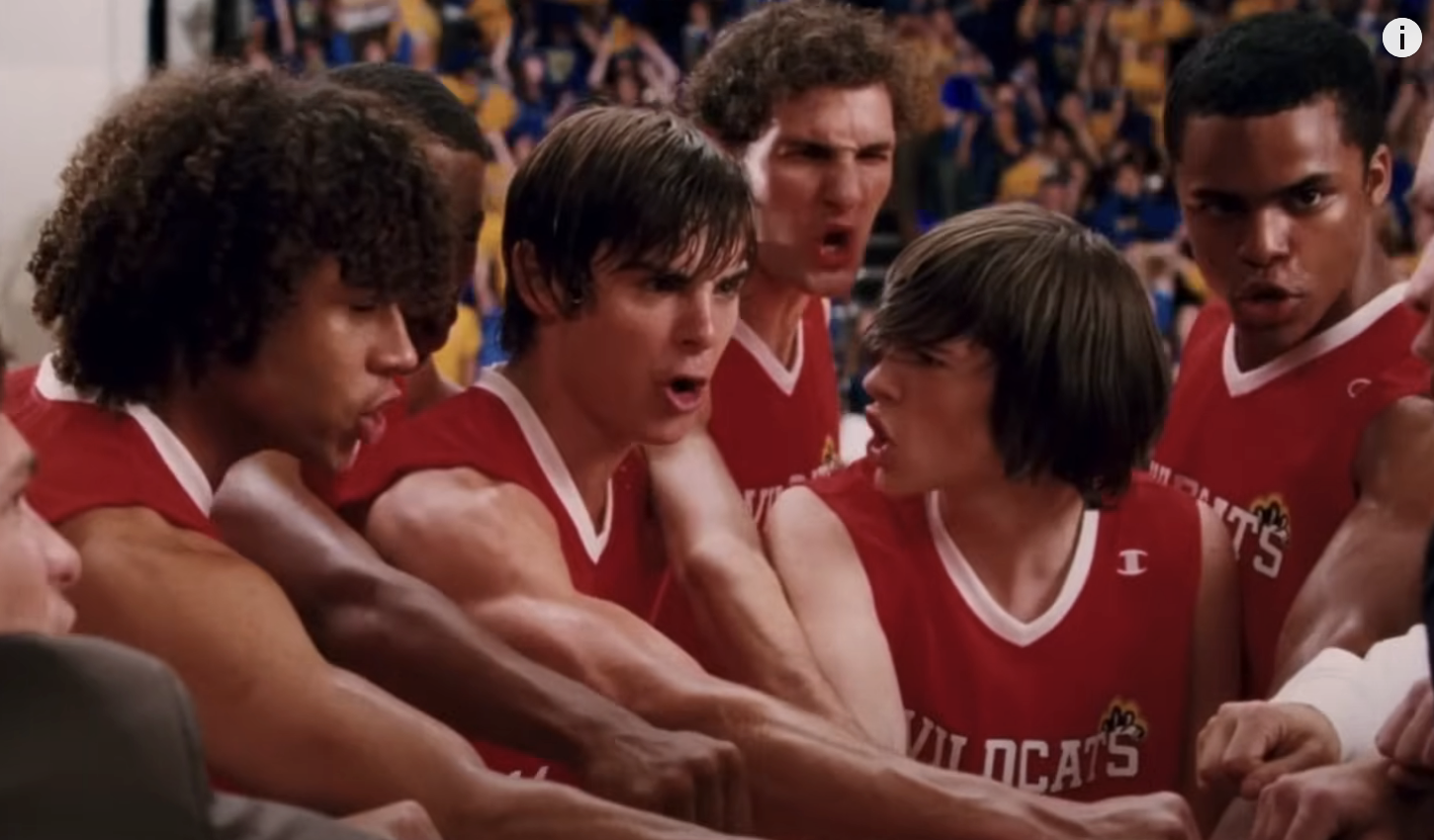 Troy, Chad, and other Wildcats in a huddle on the basketball court, looking focused