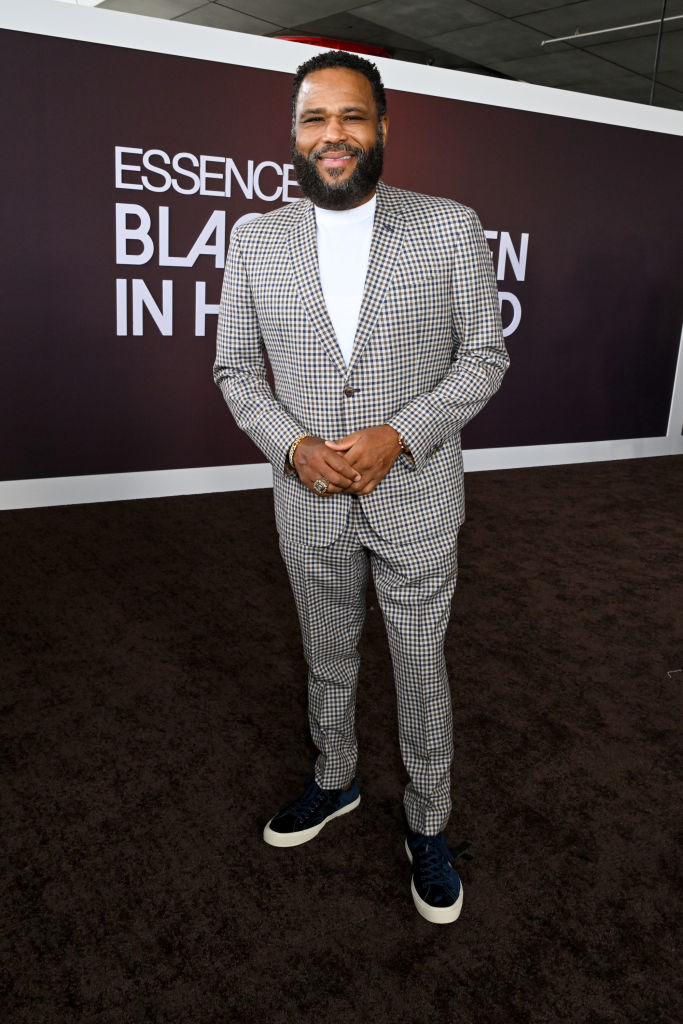 Anthony, in a checkered suit and sneakers, smiling with hands clasped