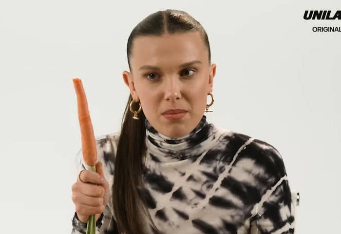Millie Bobby Brown in a tie-dye shirt holding a carrot in a YouTube video thumbnail with text and graphics