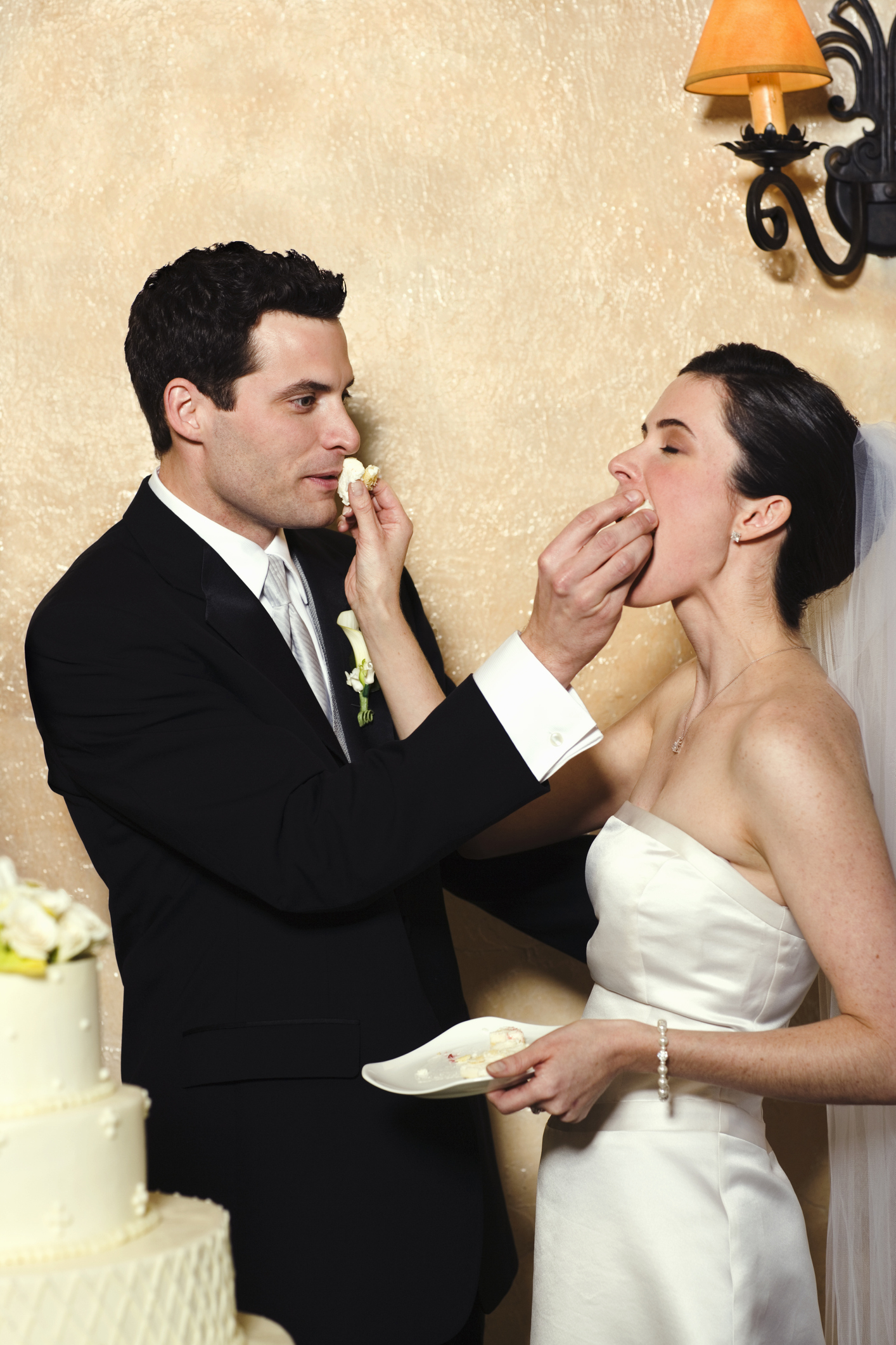 Bride in a white dress and groom in a black suit feeding each other cake at their wedding