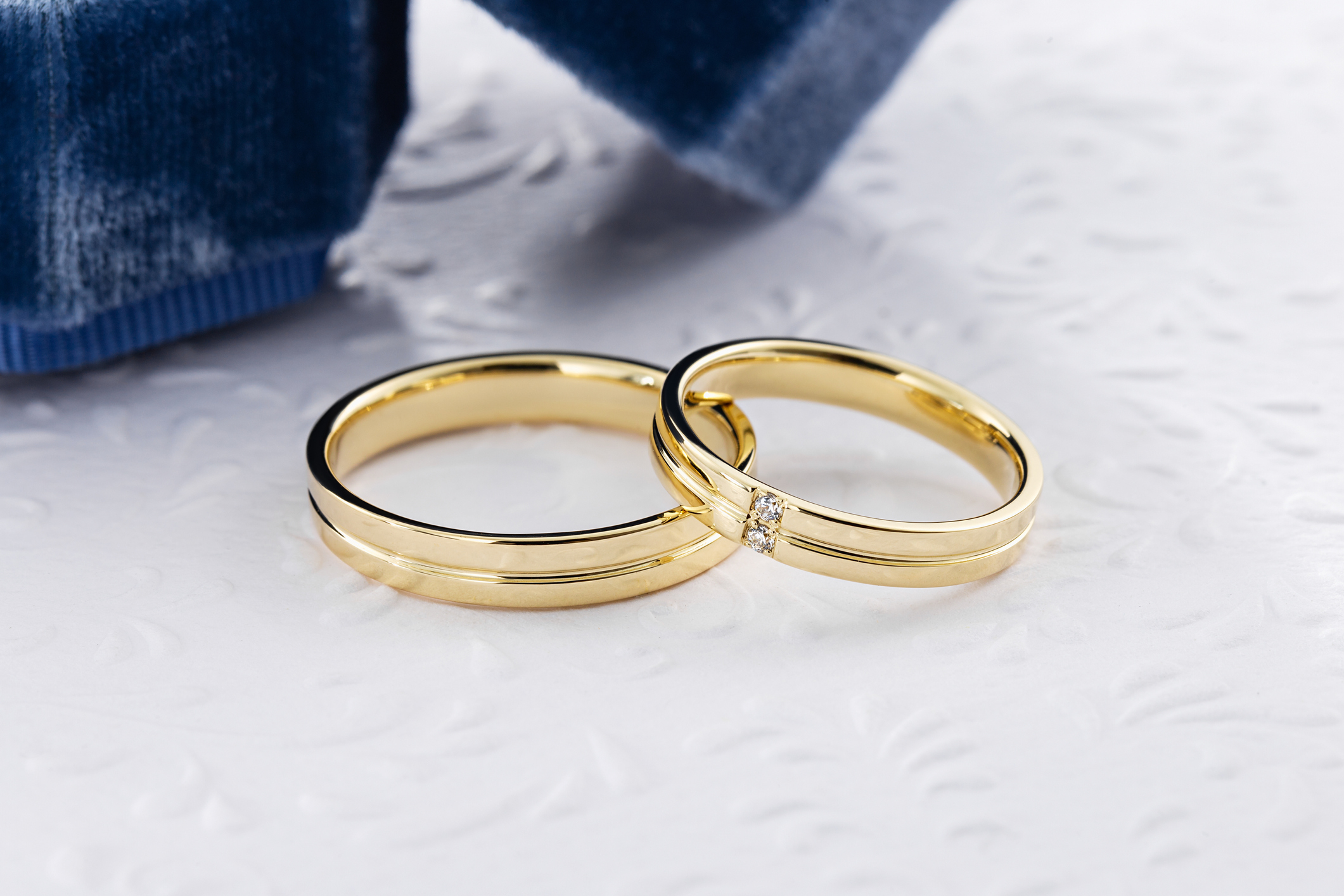 Two gold wedding bands overlapping each other on a textured surface, symbolizing union