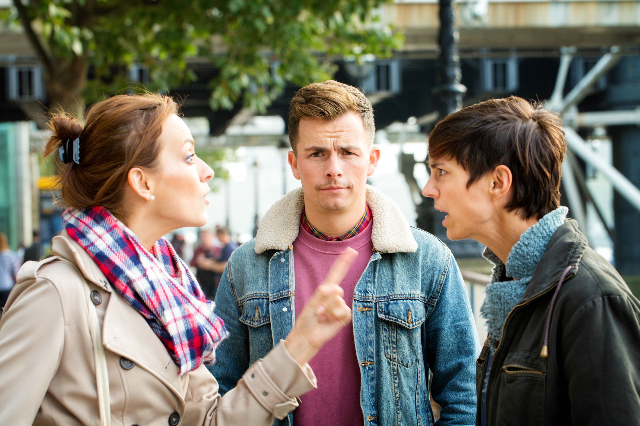 Three people appear engaged in a serious conversation, with one person seemingly uncomfortable