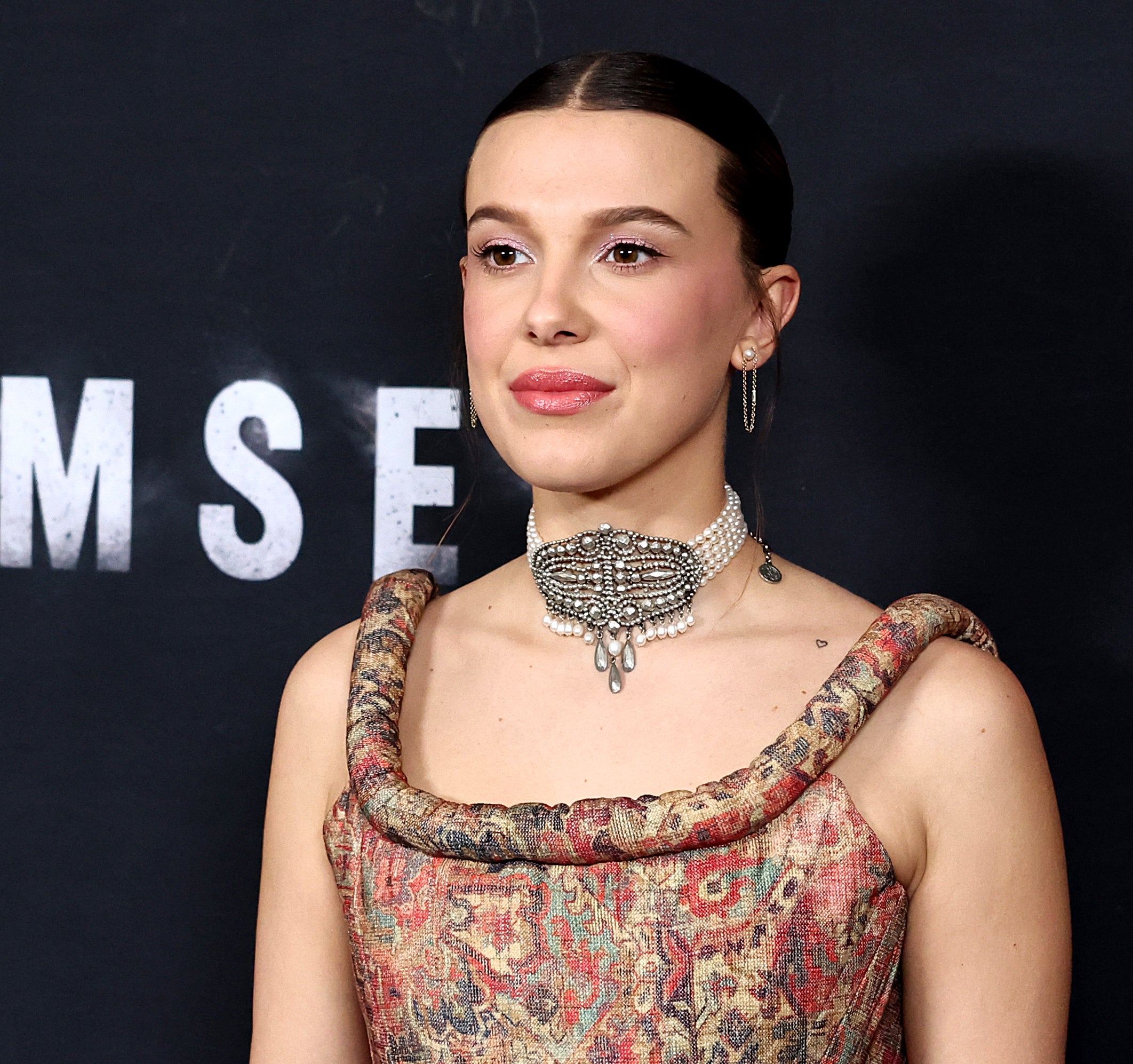 Millie wearing an ornate choker necklace and patterned dress as she poses at a media event