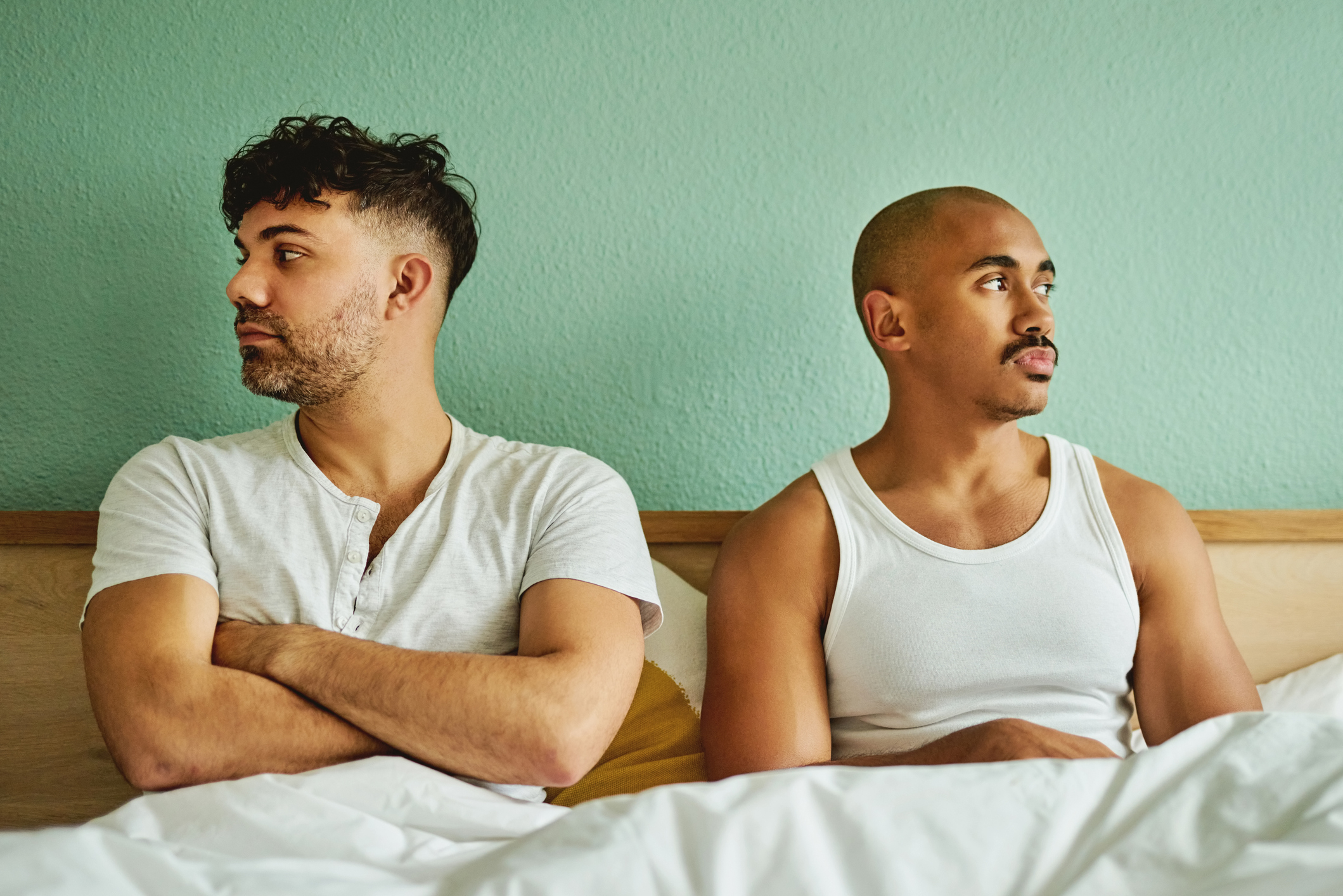 Two men sitting on a bed facing away from each other with expressions of concern or contemplation
