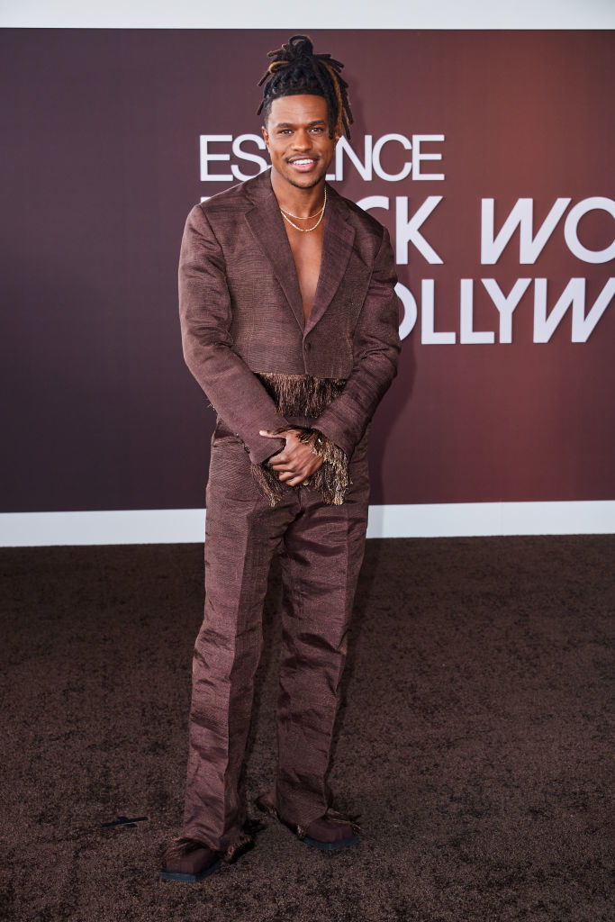 Jeremy in a textured suit sans shirt with fringe detail smiling on the red carpet