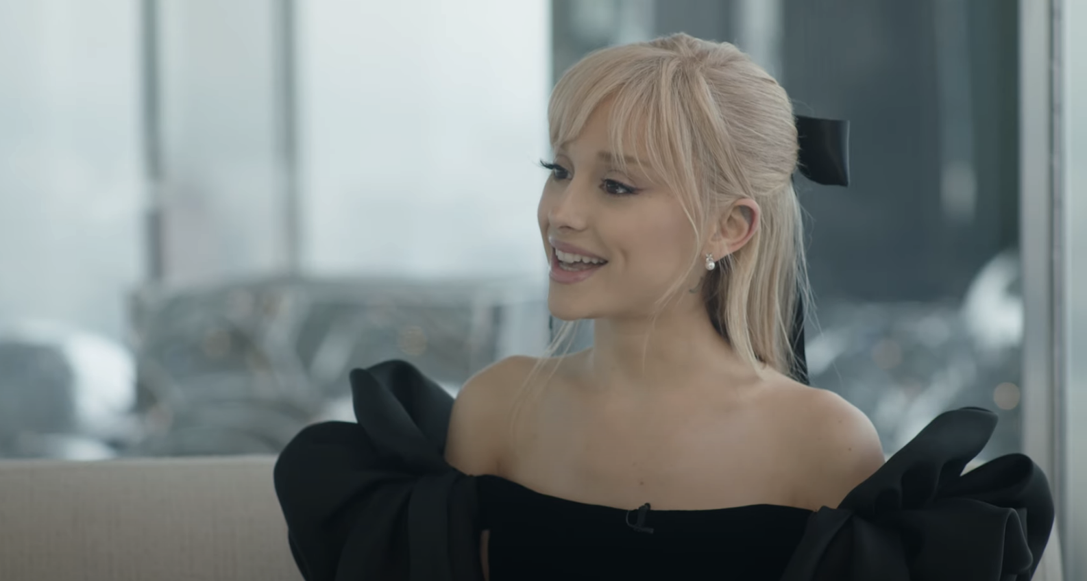 ariana in an off-shoulder dress with a bow detail, smiling and looking away