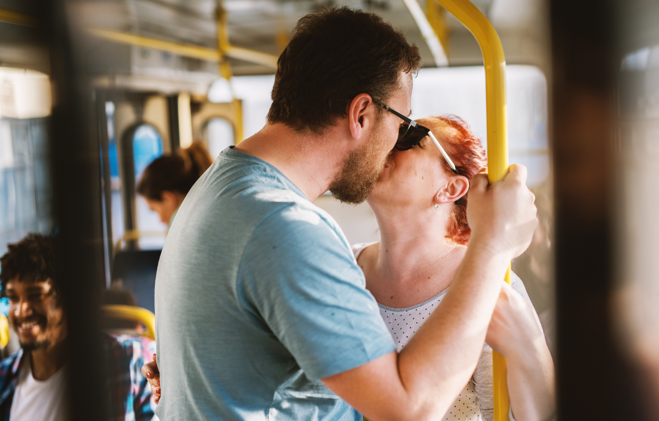 Two people sharing a kiss on a bus, others present, focus on affectionate moment