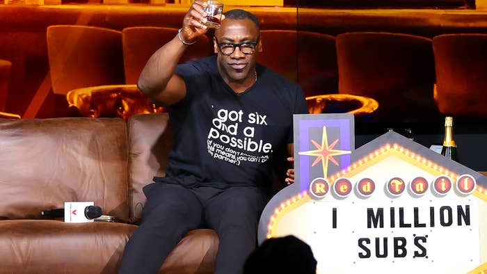 Shannon Sharpe celebrating with a toast, wearing a &quot;got six and a Possible&quot; t-shirt at a &#x27;Club Shay Shay&#x27; podcast event