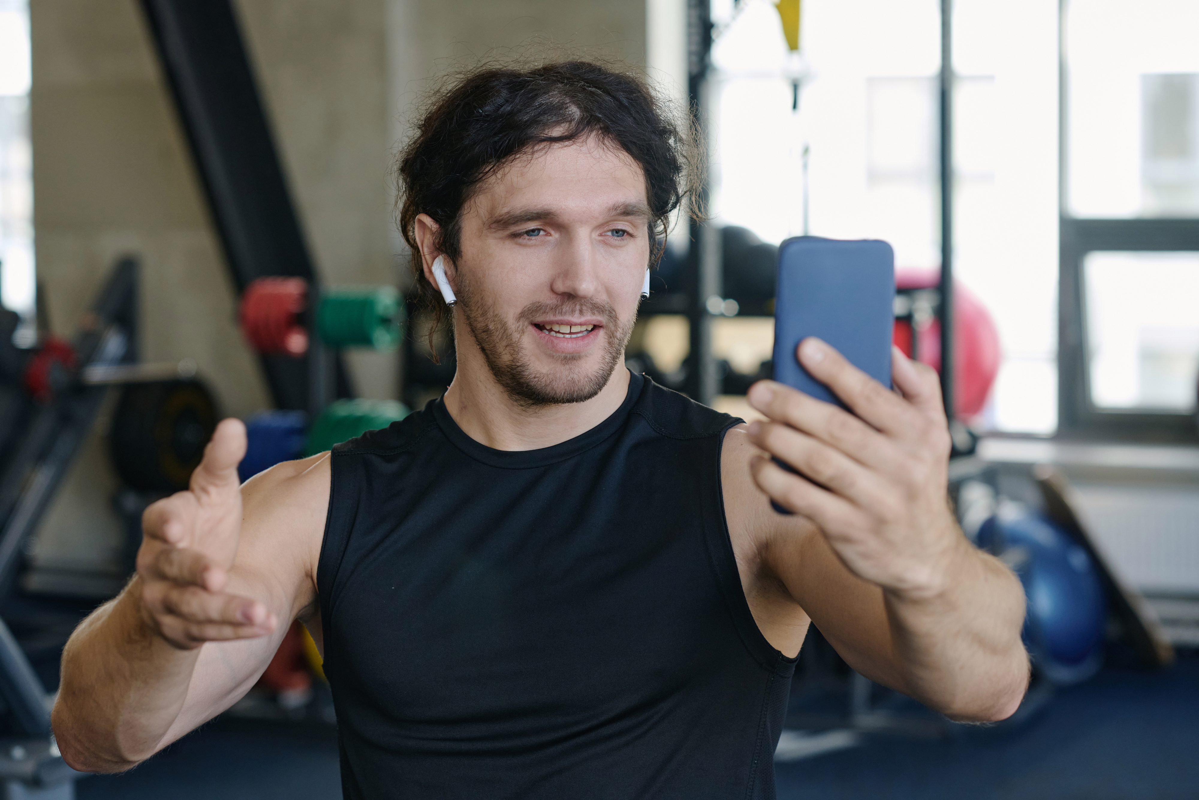 A man in sleeveless top taking a recording himself with his phone in a gym
