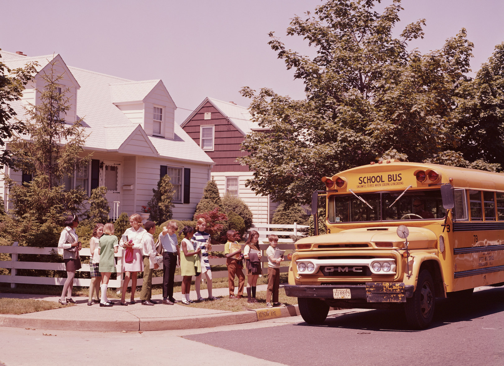 Children in a line waiting to board a school bus, daytime in a suburban setting