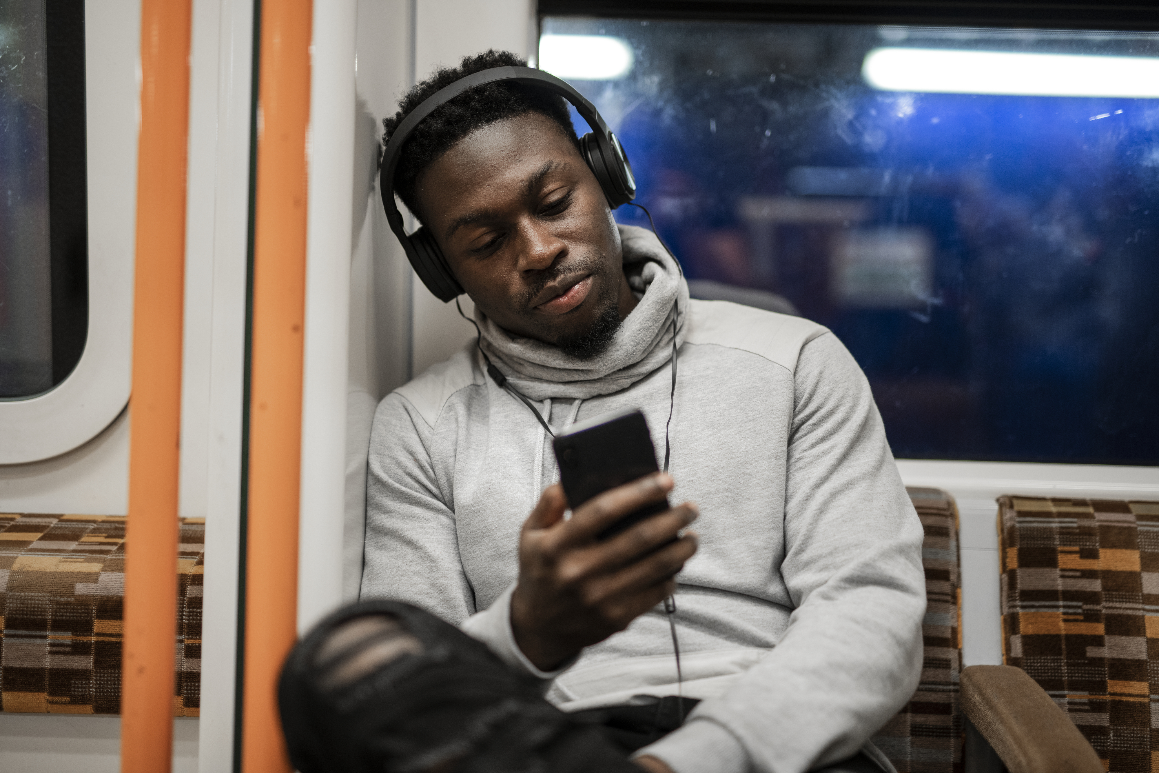 A man with headphones on using a smartphone while on public transit