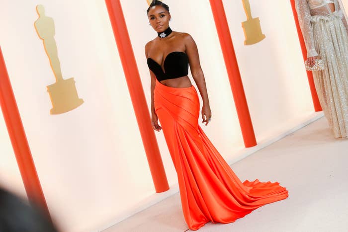 janelle monae posing in a black top and flowing orange skirt at an awards event