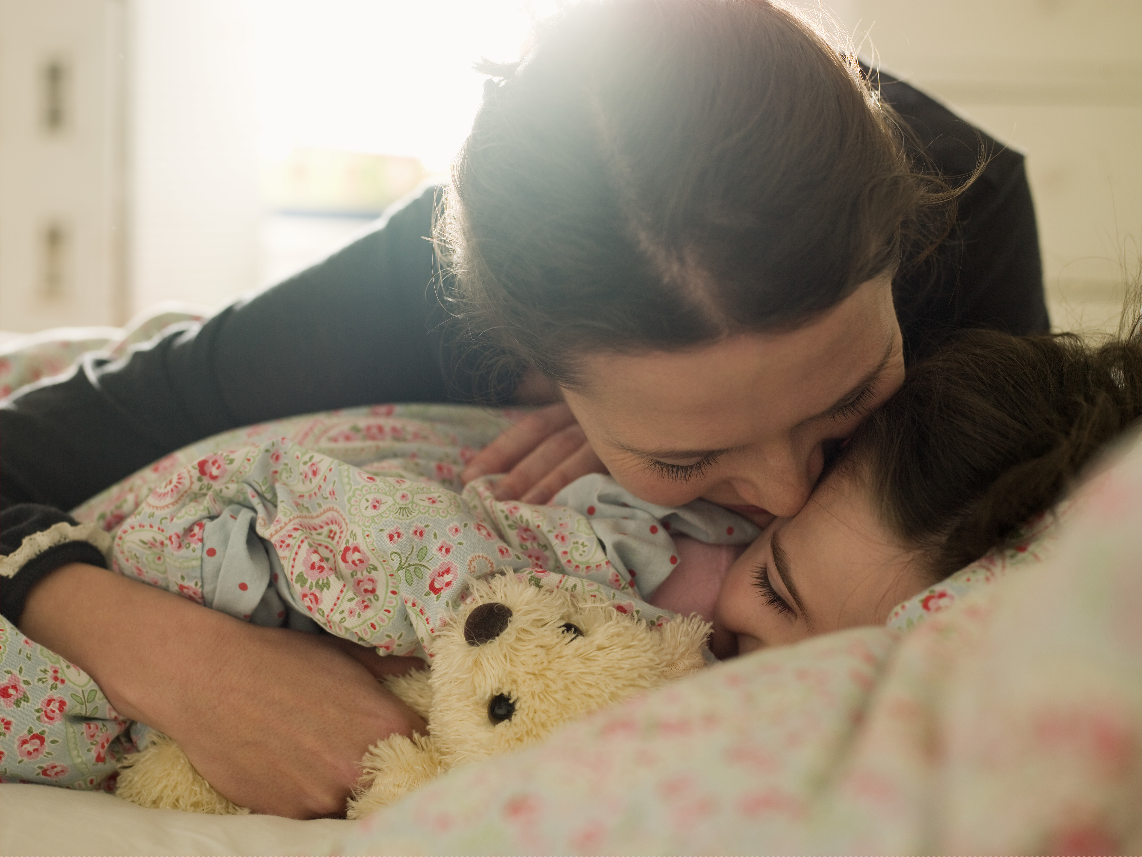 Woman and child embracing in bed with a teddy bear, sharing a tender moment