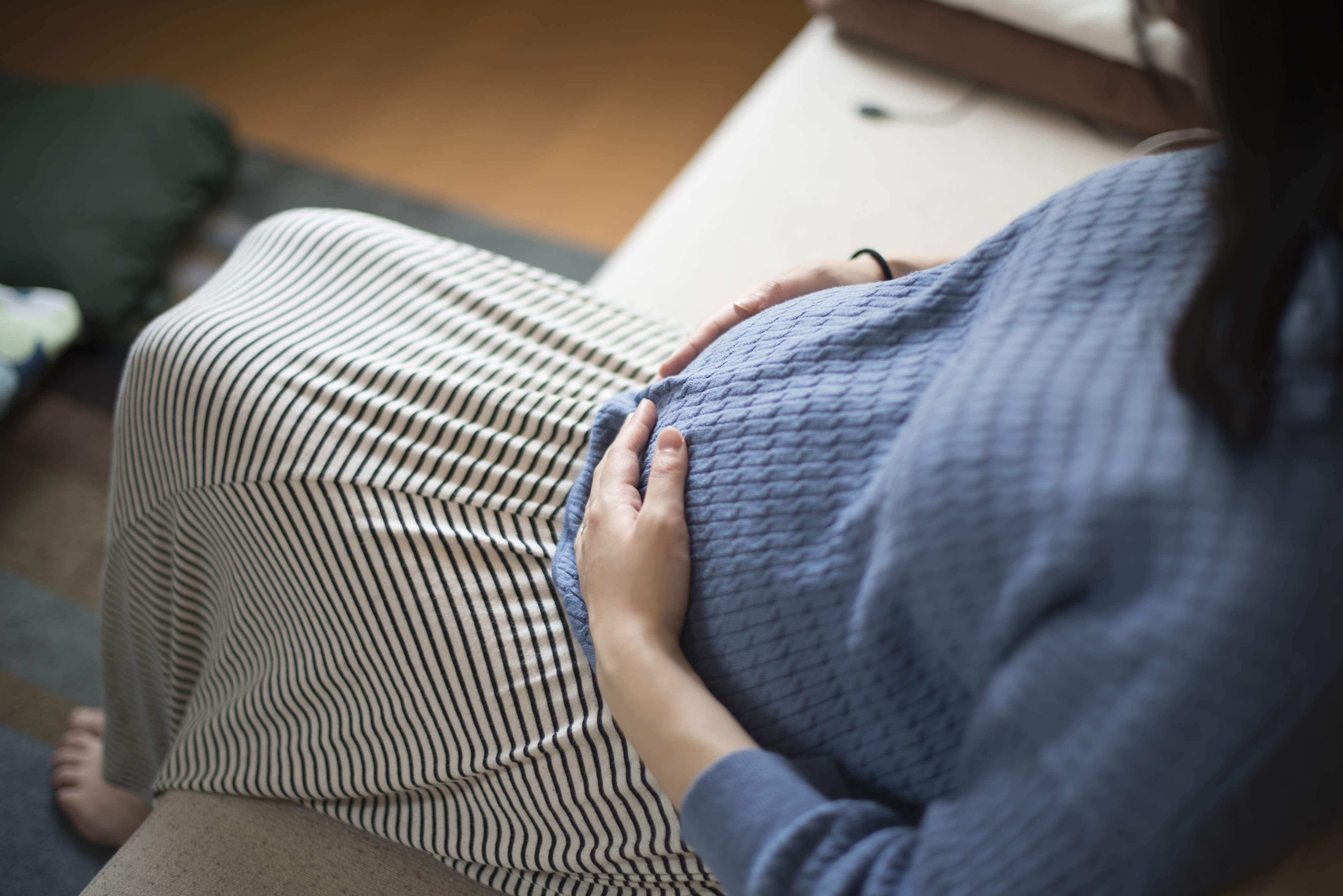 Pregnant person resting hand on belly, sitting with striped and knit fabrics visible