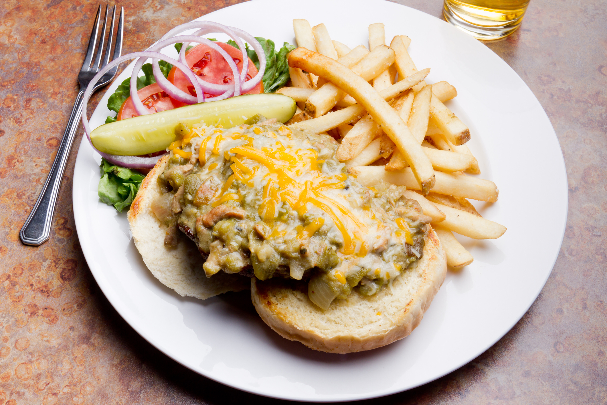 Open-faced cheeseburger with fries and salad on a plate, beside a glass of beverage
