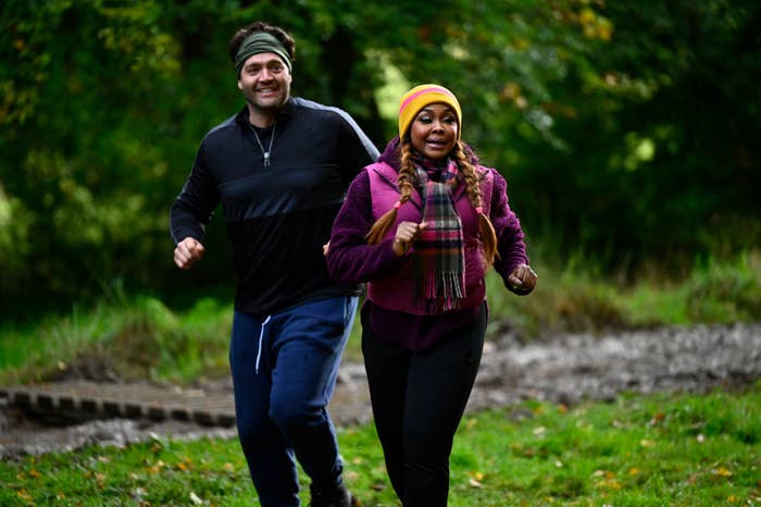 Two people jogging in a park, one in a black top and beanie, the other in a purple jacket and yellow beanie