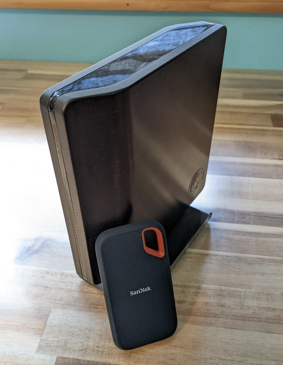 A standing external hard drive leaning against an upright computer monitor on a wooden surface