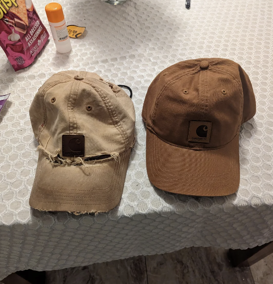 Two worn baseball caps with carhartt logos on a table, indicating parenting and everyday life