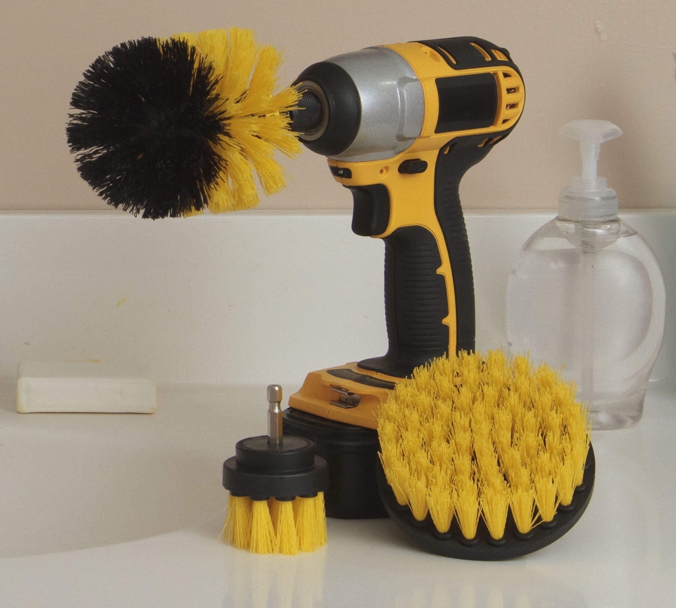 Drill with attached scrub brush next to additional brush heads and a soap dispenser
