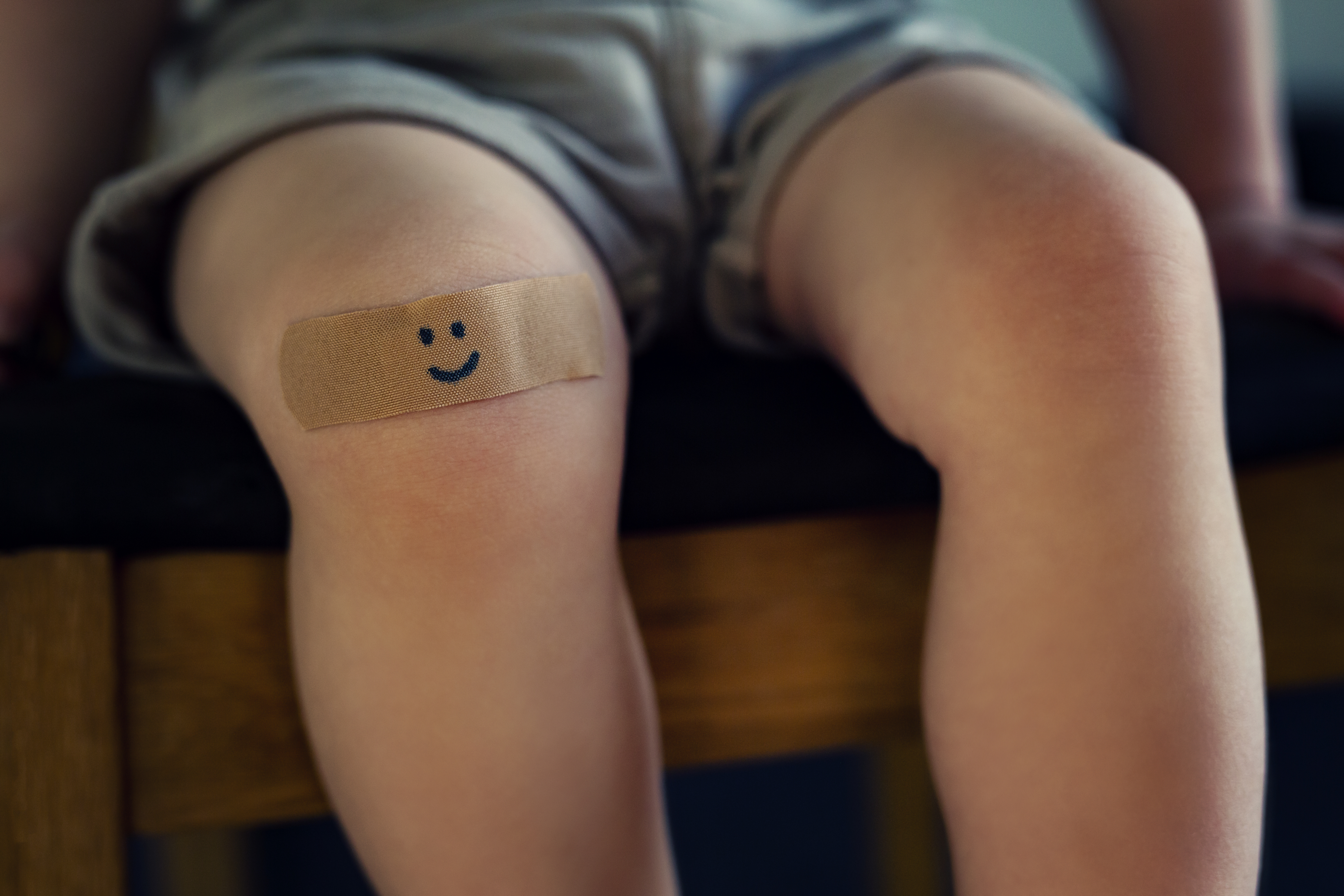 Child seated with a smiley-face bandage on the knee