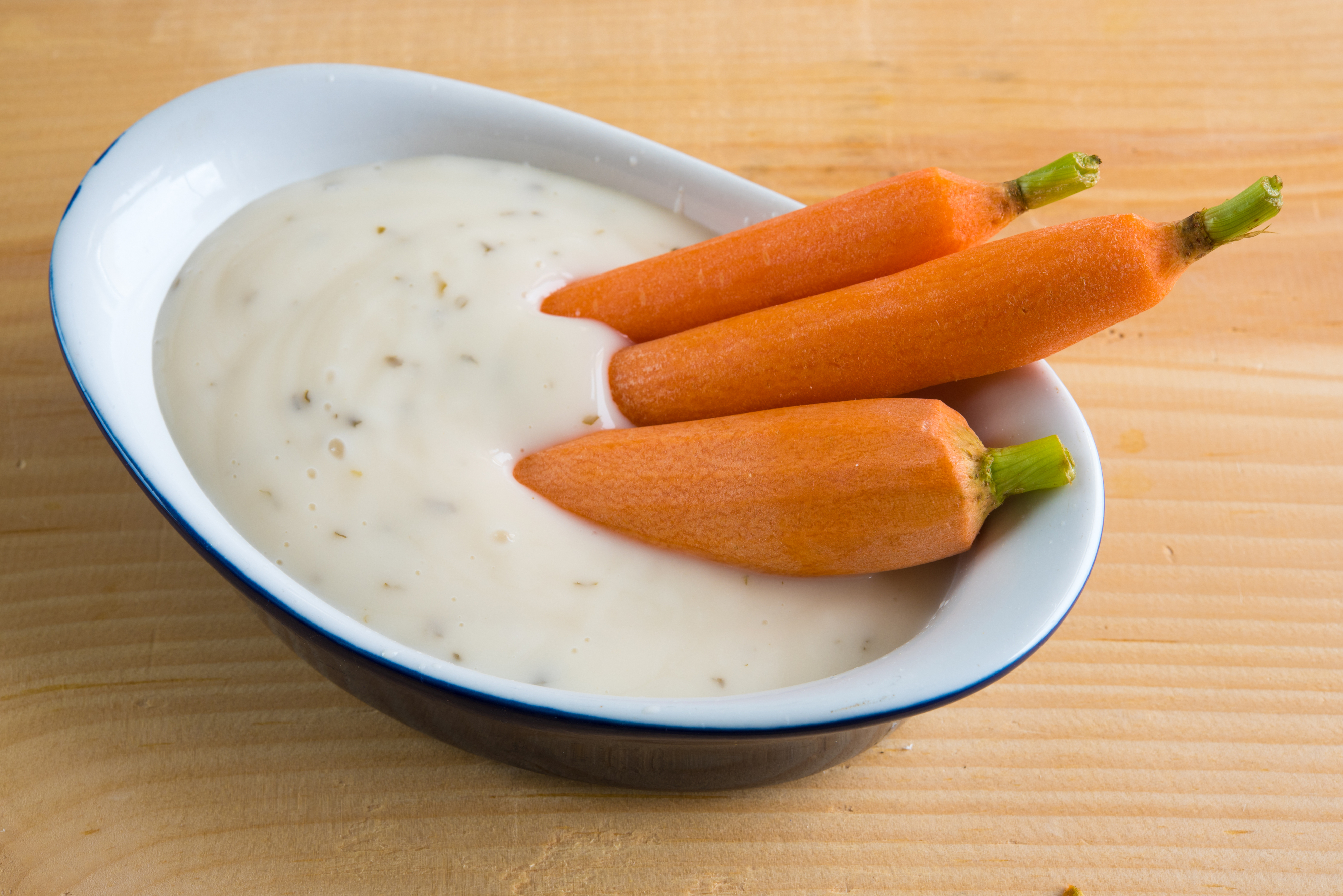 Three whole carrots in a bowl of dip on a wooden surface