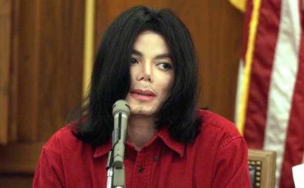 Michael Jackson sits wearing a red shirt, speaking into a microphone in a courtroom setting