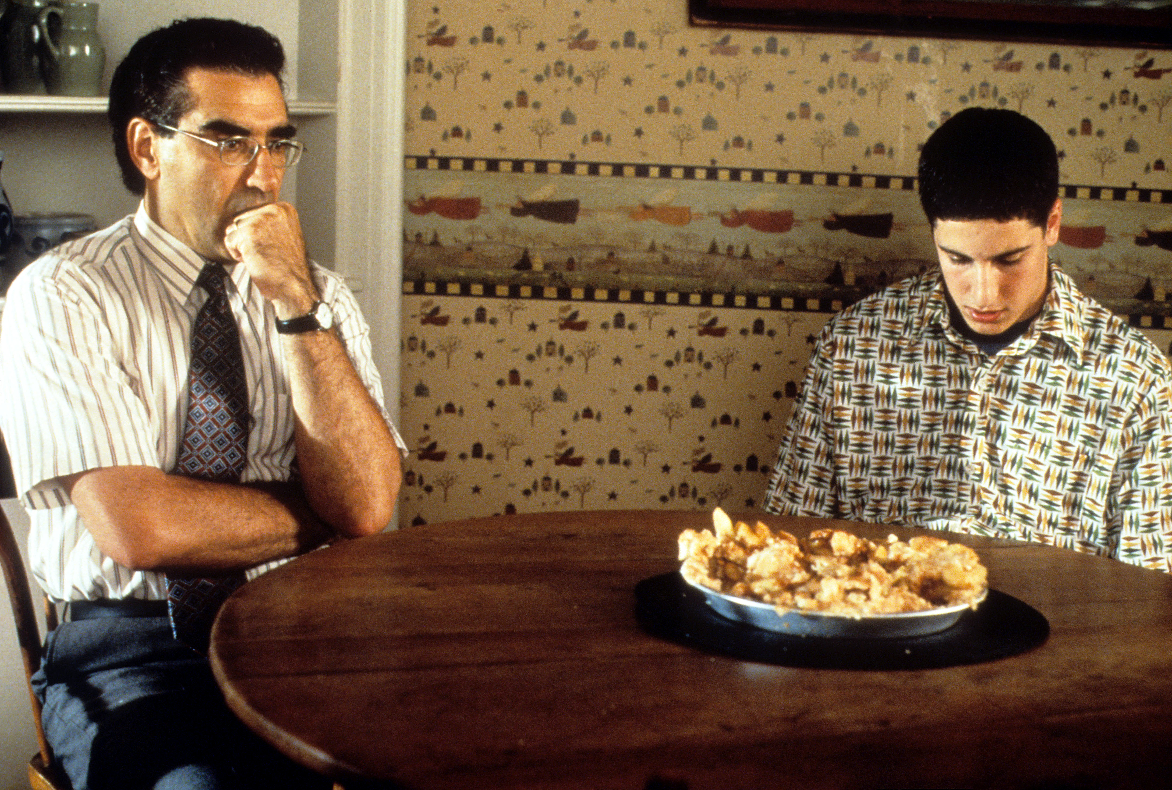 Eugene Levy and Jason Biggs sit at a table with a pie in the film &quot;American Pie.&quot;