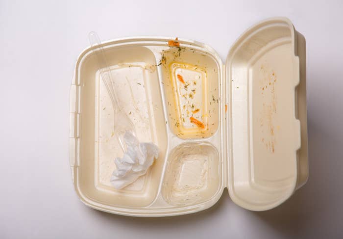 An empty food takeout container with remnants and a used napkin, indicating a finished meal