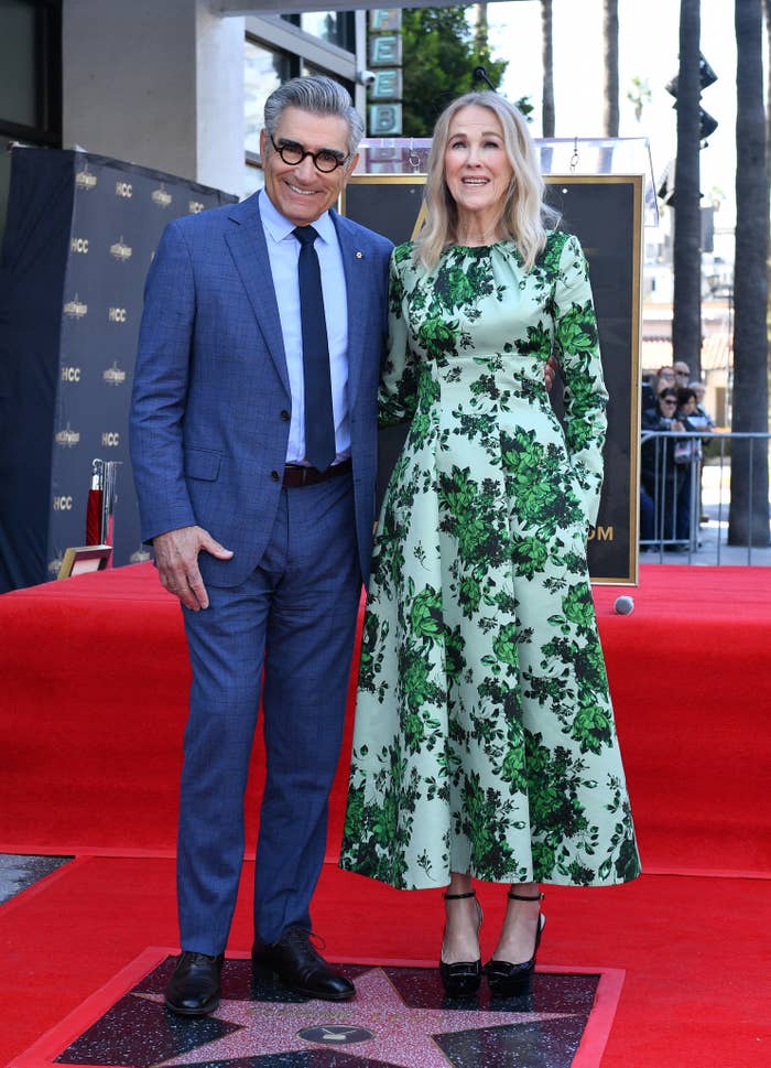 Eugene Levy and Catherine O&#x27;Hara stand side by side by his star; she wears a floral dress, he&#x27;s in a suit