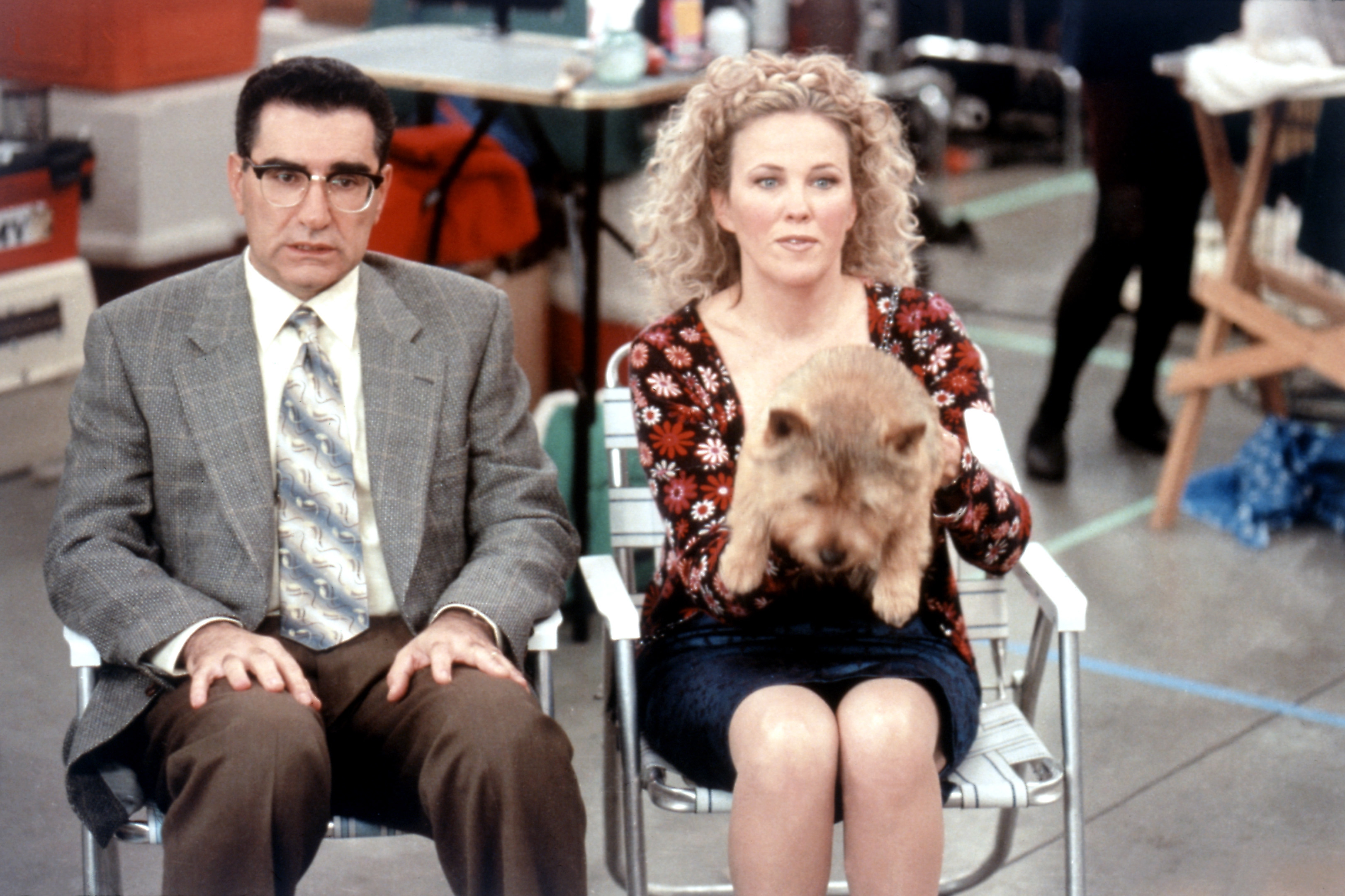 Eugene Levy and Catherine O&#x27;Hara sit side by side with a small dog on Catherine&#x27;s lap in a scene from a film