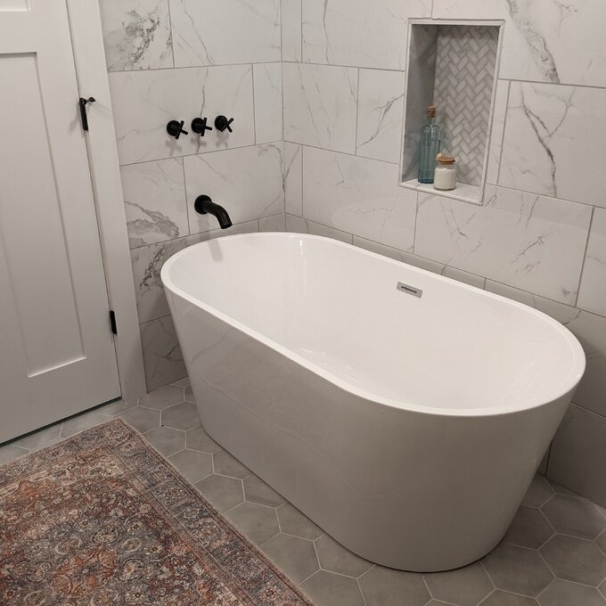 a reviewer photo of the freestanding white bathtub in a tiled bathroom with a herringbone accent niche and Persian rug
