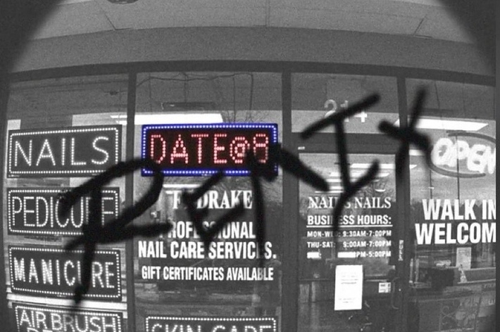 The image shows a neon sign for a nail salon with the word "DATE???" displayed, viewed through a barbed wire fence