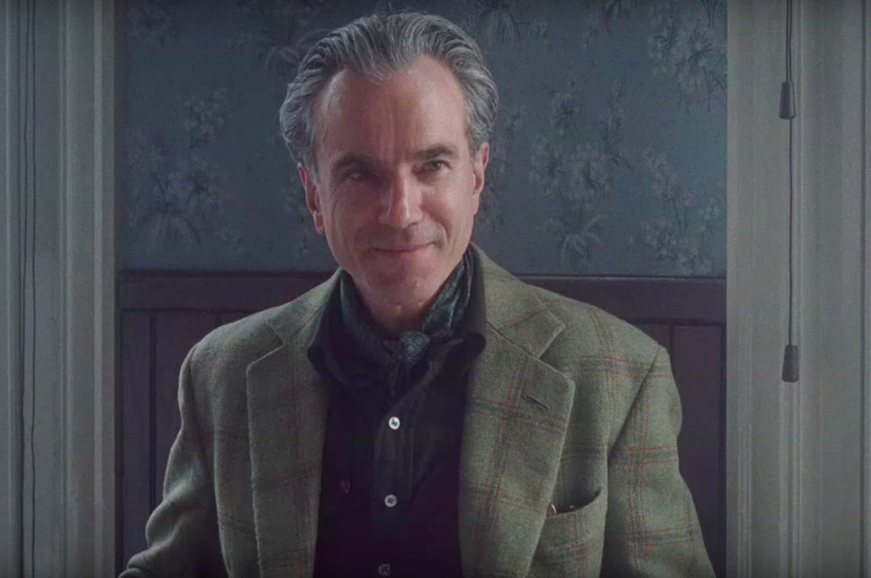 Daniel Day-Lewis in a tweed blazer and green scarf, seated, facing the camera with a subtle smile