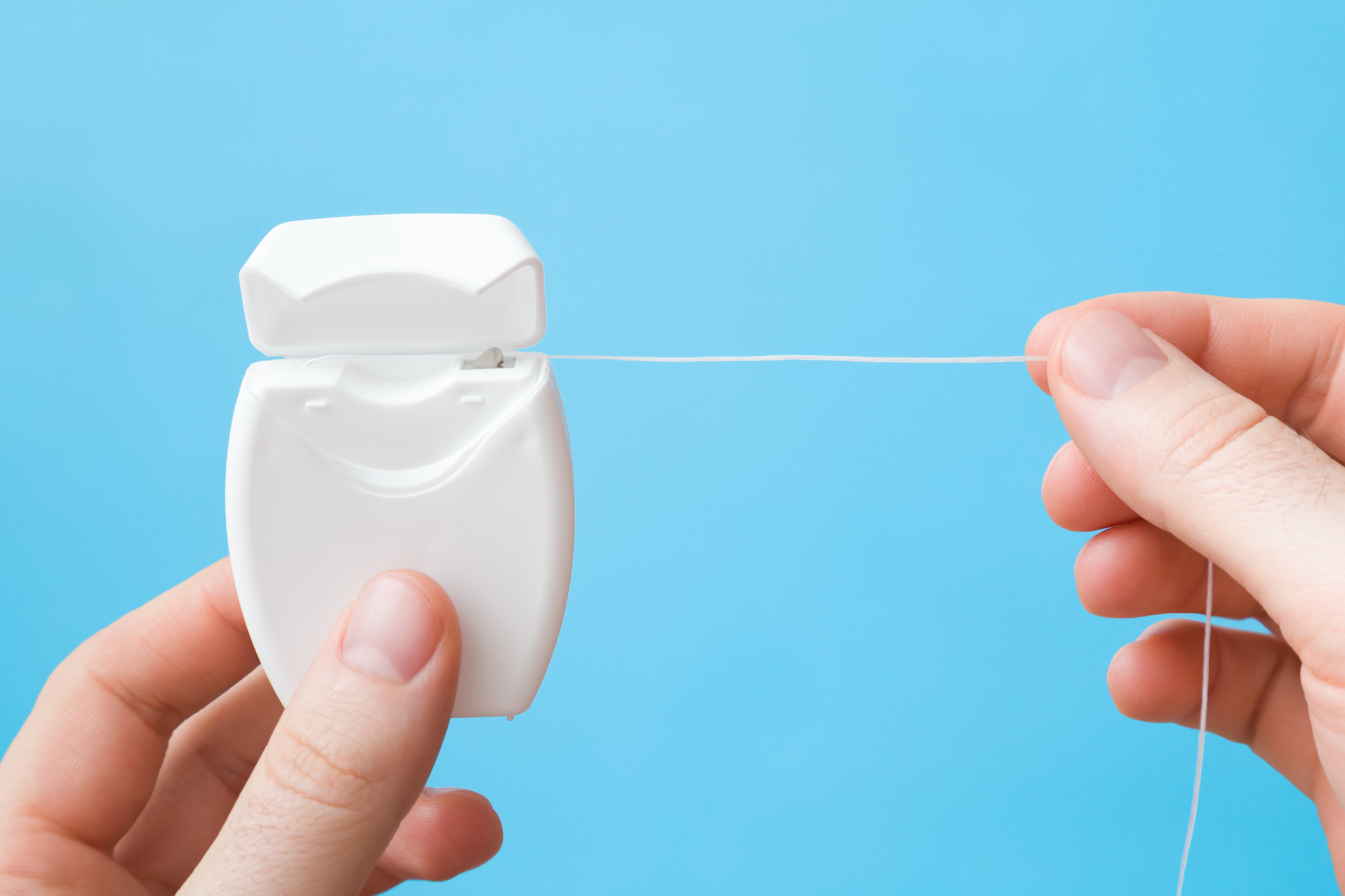Two hands using dental floss from a white dispenser against a blue background