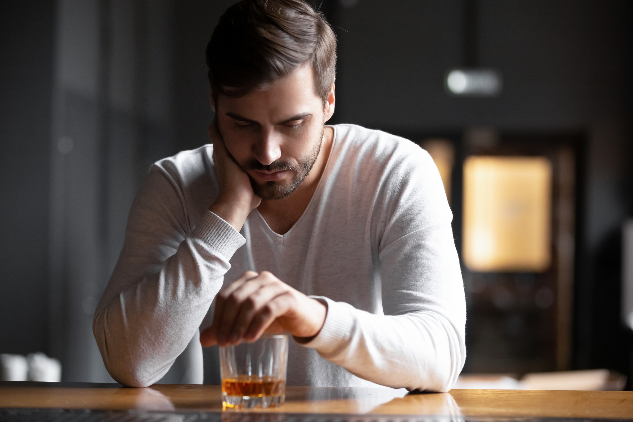 Man sitting at a table with his head resting on his hand, looking at a glass of whiskey