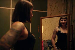 鏡に向かって立つタトゥーのある女性がブラックドレスを着用している。