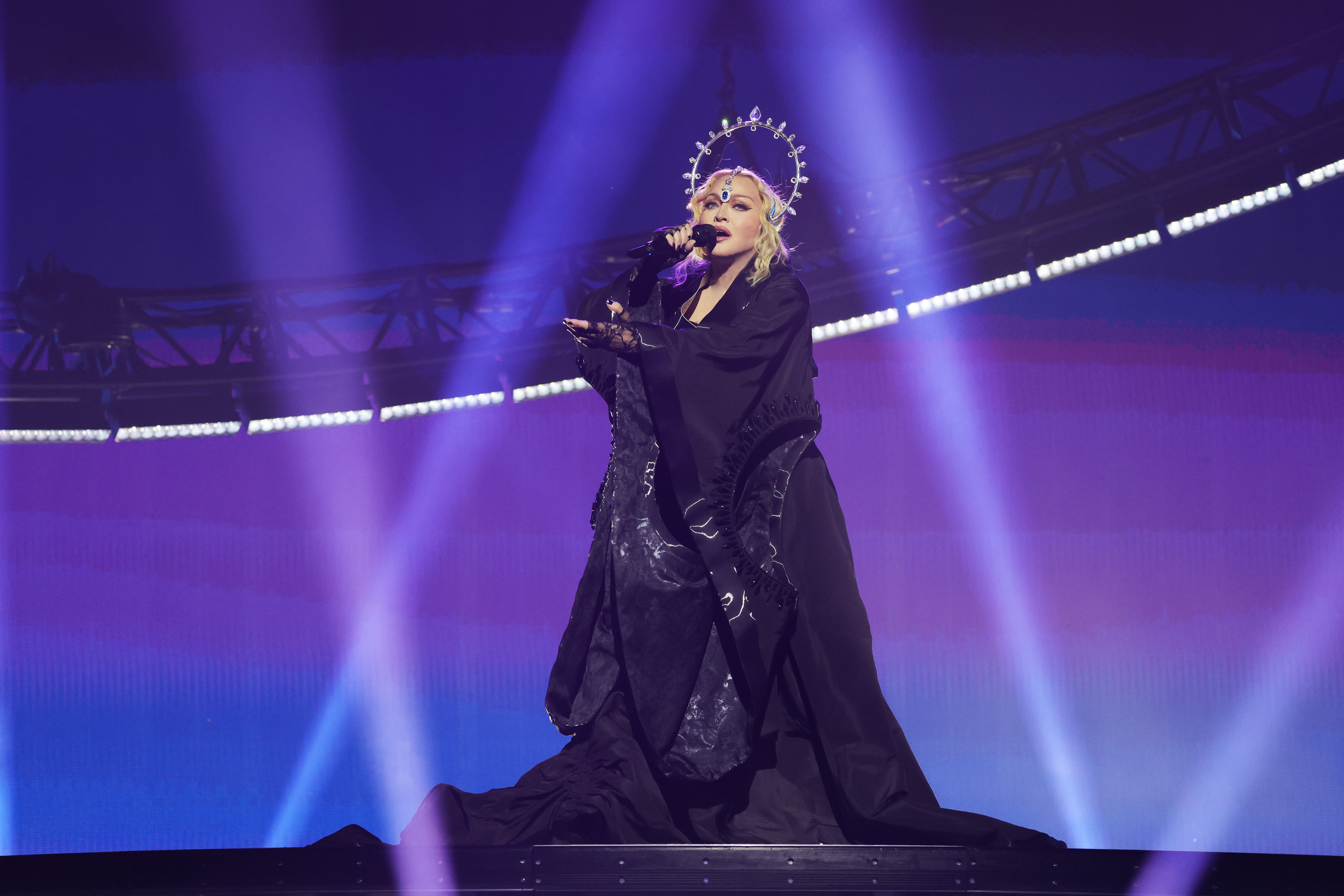 Madonna in an embellished halo-lie headpiece and robe sings onstage