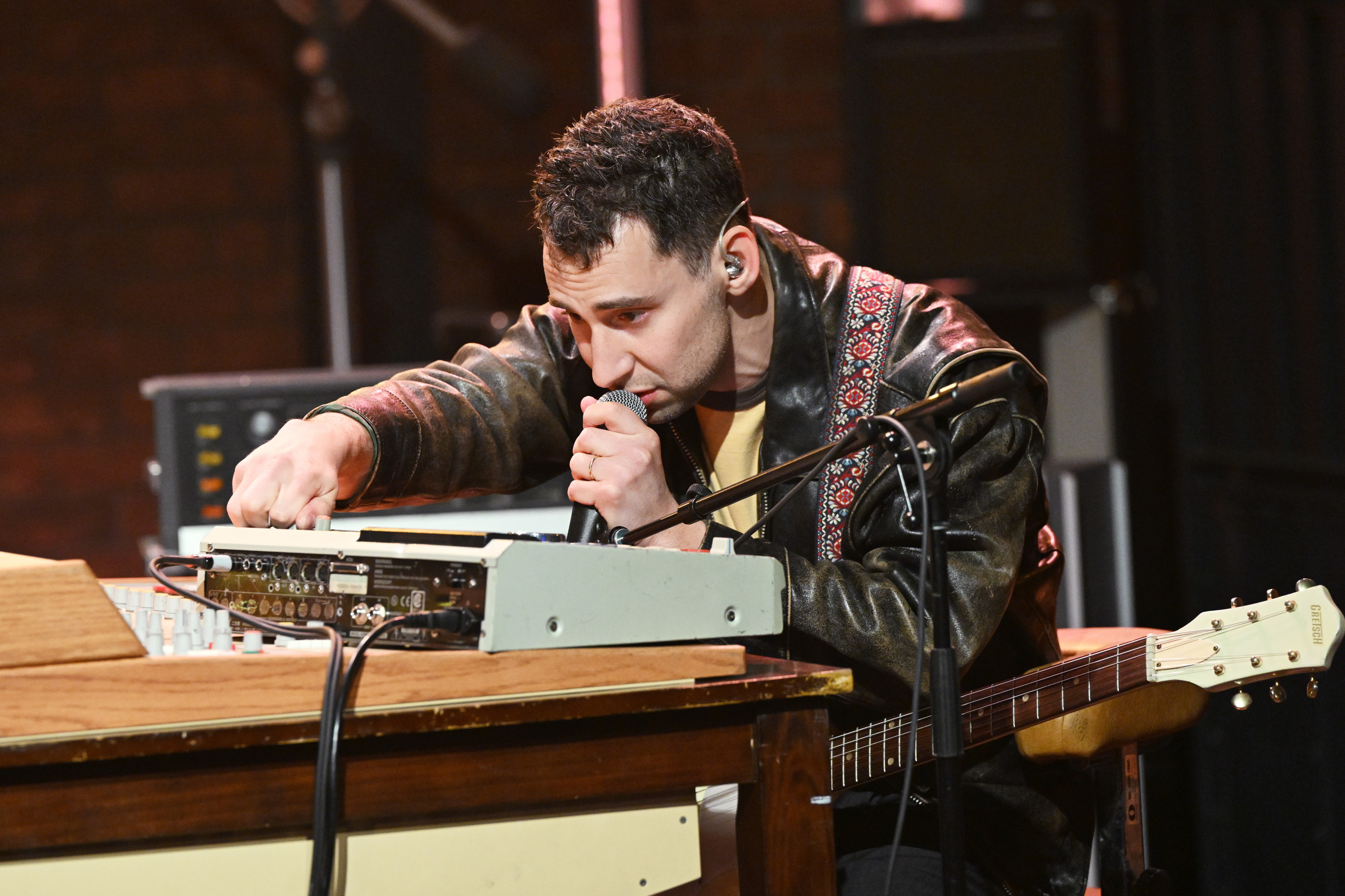 jack at a keyboard with a microphone, wearing a leather jacket, engaged in producing